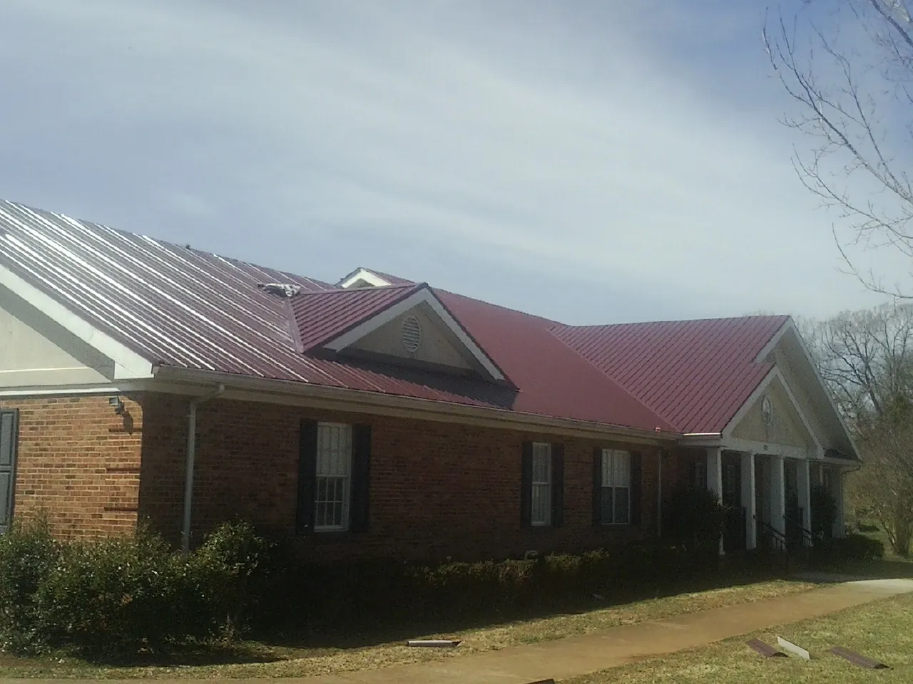 Red metal roof with gabled entries on a long brick building, from a Hail Damage Roof Repair job in Adams Run