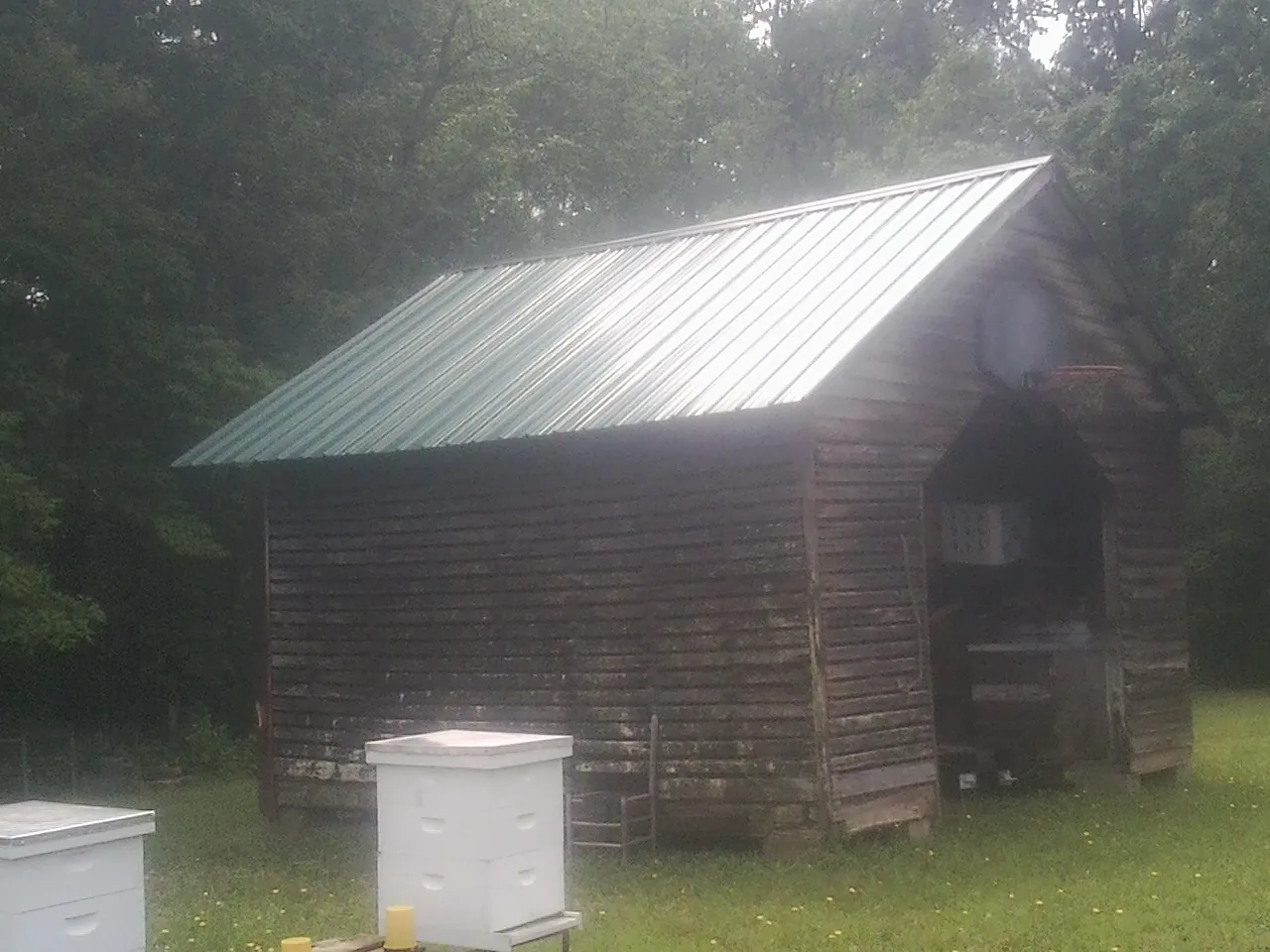Green metal roof on a weathered barn beside stacked beehives in Adams Run