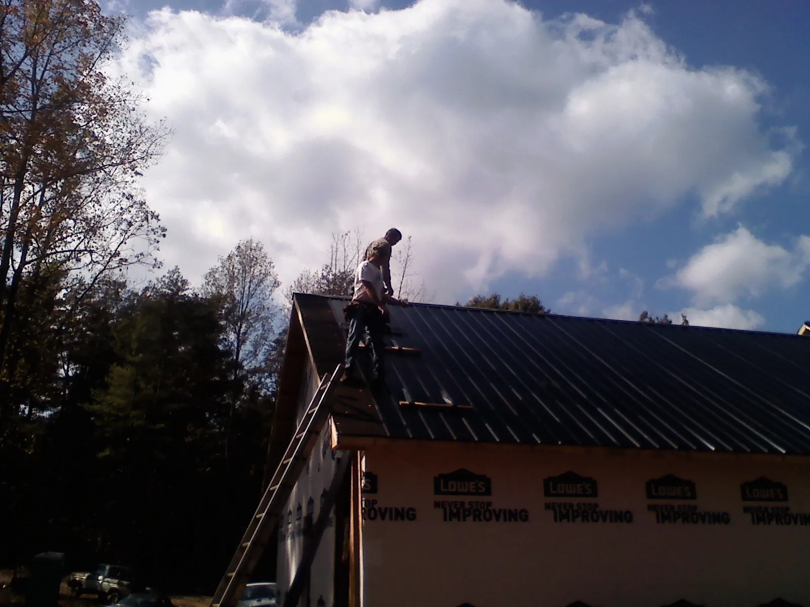 Roofer fastening dark metal panels high against a cloudy sky, from a Roof Inspection job in Adams Run