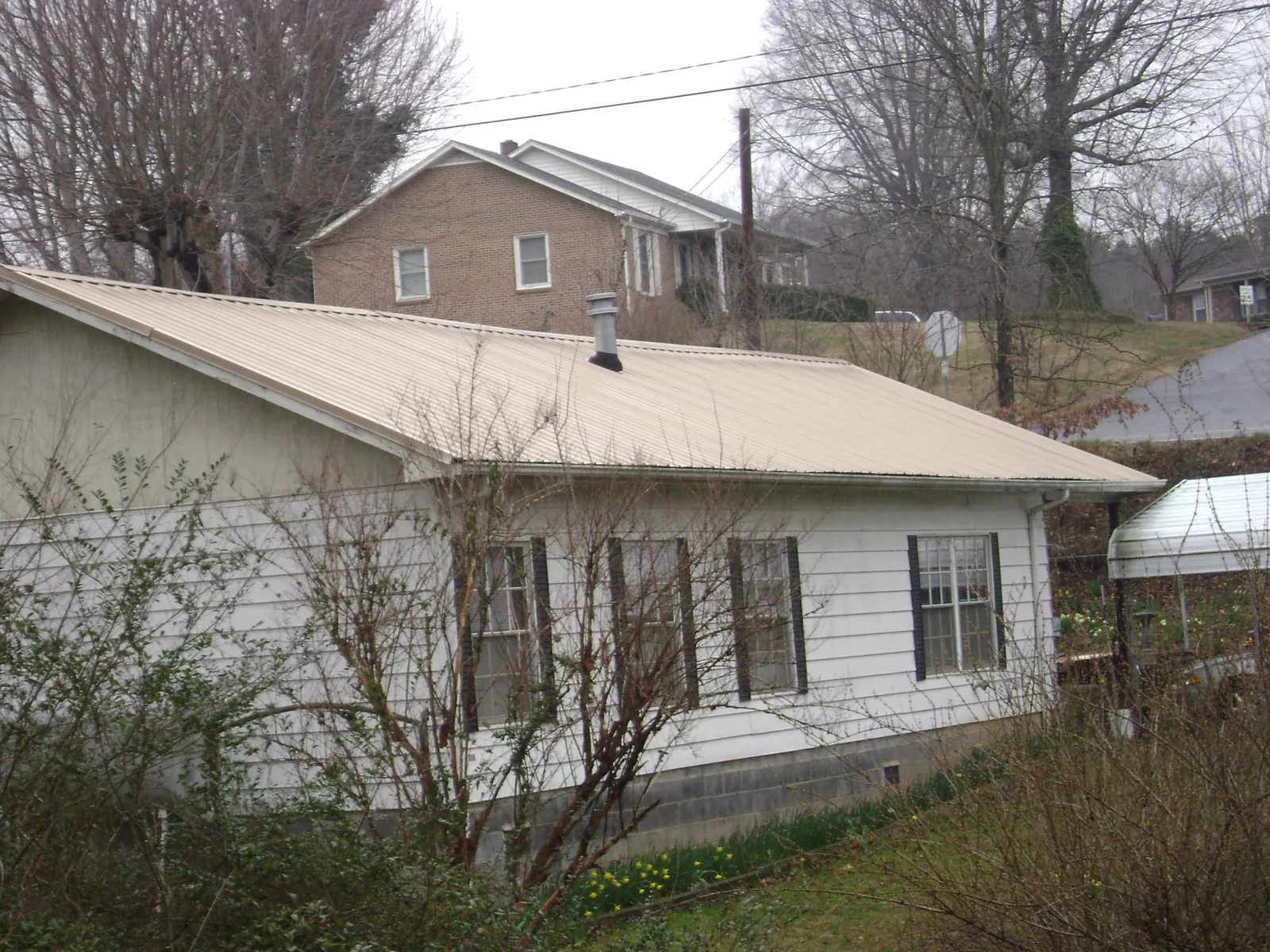 Tan metal roof on a white sided house set into a hillside — Commercial Roofing by Roofing Brothers in Adams Run